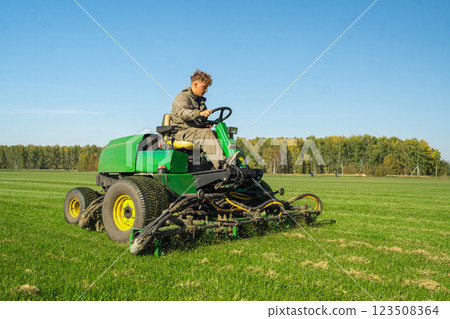 A farmer mows lush grass with a green tractor, embodying agriculture and rural charm 123508364