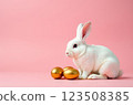White rabbit sitting next to golden easter eggs on pink background  123508385