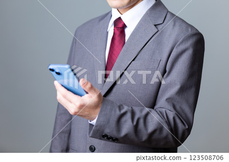 身穿灰色西裝、手持智慧型手機的中年男性商人 身穿灰色西裝、手持智慧型手機的中年男性商人 123508706