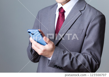 A middle-aged male businessman wearing a gray suit and holding a smartphone A middle-aged male businessman wearing a gray suit and holding a smartphone 123508707