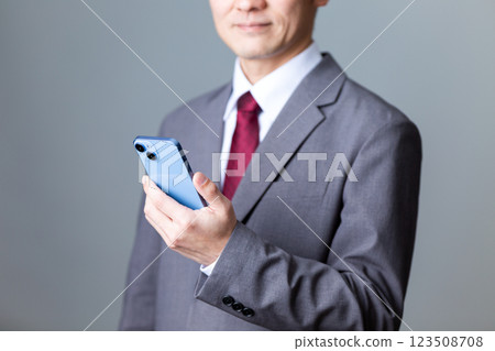 A middle-aged male businessman wearing a gray suit and holding a smartphone 123508708