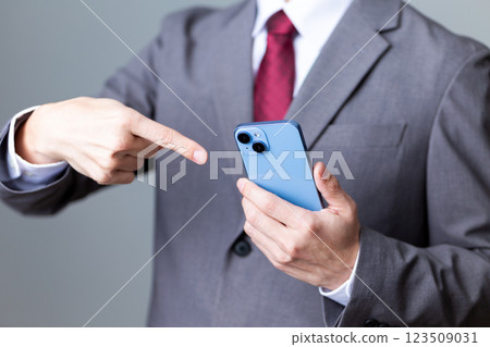 A middle-aged male businessman wearing a gray suit and pointing at a smartphone A middle-aged male businessman wearing a gray suit and pointing at a smartphone 123509031