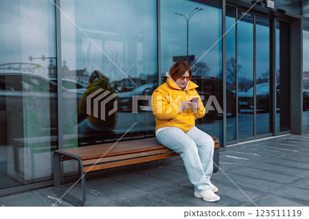 Portrait of happy smiling Caucasian woman, sitting outdoors near building, using smartphone. Technology concept. 123511119