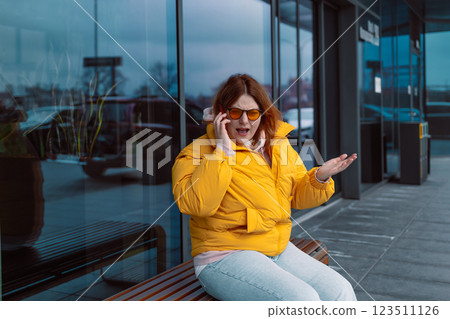 Negative emotions. Angry young woman wearing a yellow jacket and sunglasses talking over phone disappointed hear bad news, sad pensive girl speaking having unpleasant smartphone conversation and Negative emotions. Angry young woman wearing a yellow jacket and sunglasses talking over phone disappointed hear bad news, sad pensive girl speaking having unpleasant smartphone conversation and 123511126