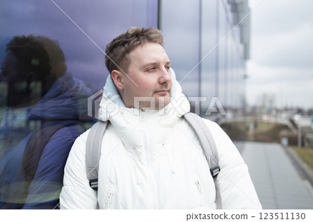 Portrait of Caucasian smiling bearded man with backpack, looking at camera aganist airport terminal building in the winter city. Lifestyle, city life concept 123511130