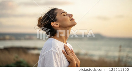 A close profile shot of a person gently placing their hand on their chest while taking a deep breath. This highlights the connection between breath and physical sensation. 123511500