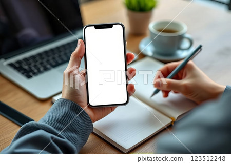Person Using AI Assistant on Smartphone While Taking Notes at a Workspace 123512248