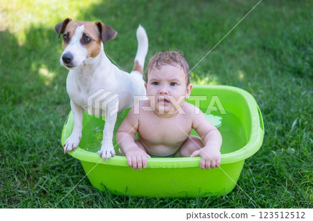 Cute boy bathes in a basin with a Jack Russell terrier dog outdoors in the summer. Cute boy bathes in a basin with a Jack Russell terrier dog outdoors in the summer. 123512512