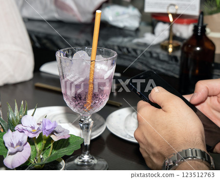 A glass with a cocktail and men's hands hold a phone. A glass with a cocktail and men's hands hold a phone. 123512763