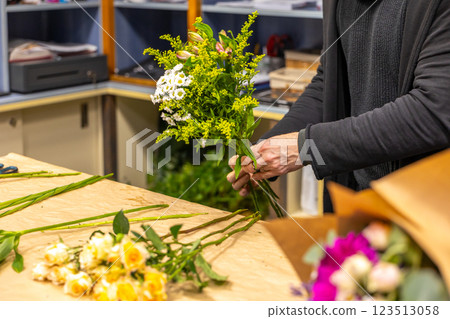 Florist arranging bouquet with lilies and solidago in flower shop 123513058