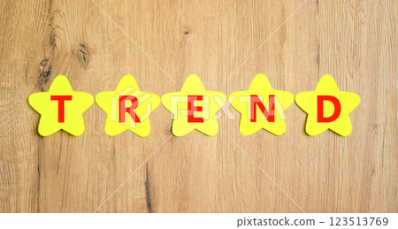 Trend and trending symbol. Concept word Trend on beautiful yellow paper stars. Beautiful wooden table wooden background. Business lifestyle trend and trending concept. Copy space. Trend and trending symbol. Concept word Trend on beautiful yellow paper stars. Beautiful wooden table wooden background. Business lifestyle trend and trending concept. Copy space. 123513769