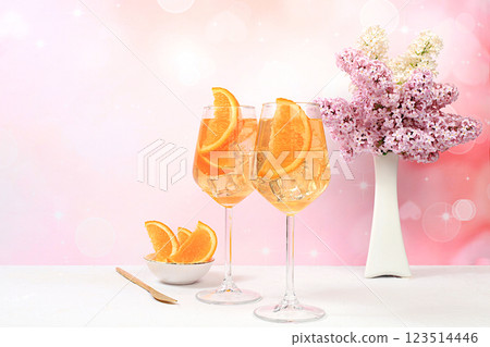Festive alcoholic cocktail Aperol spritz in glasses on a bright background with a bouquet of lilacs, summer bar concept, alcoholic drinks at a party, restaurant and cafe advertising, selective focus 123514446