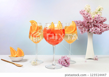 Festive alcoholic cocktail Aperol spritz in glasses on a bright background with a bouquet of lilacs, summer bar concept, alcoholic drinks at a party, restaurant and cafe advertising, selective focus 123514447