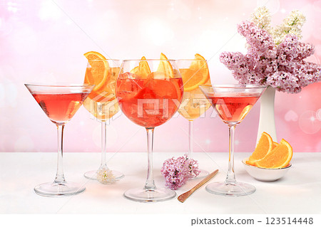 Festive alcoholic cocktail Aperol spritz and red martini in glasses on a bright background with a bouquet of lilacs, summer bar concept, alcoholic drinks at a party, restaurant and cafe advertising, 123514448