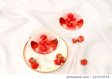 Festive alcoholic cocktail, red martini in glasses on a bright background with strawberries, summer bar concept, alcoholic drinks at a party, restaurant and cafe advertising, selective focus. Festive alcoholic cocktail, red martini in glasses on a bright background with strawberries, summer bar concept, alcoholic drinks at a party, restaurant and cafe advertising, selective focus. 123514554