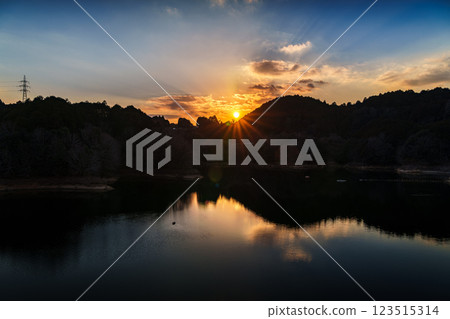 The temperature is rising and it's starting to feel like spring at Nara Nunome Dam. The sun sets over the mountains on the opposite shore, painting the sky and lake surface golden. 123515314