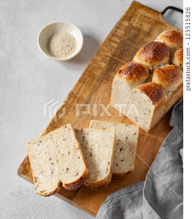 Freshly baked whole grain bread with slices on a wooden board with a sesame seeds and napkin Freshly baked whole grain bread with slices on a wooden board with a sesame seeds and napkin 123515826