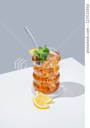 Iced tea with lemon, ice and mint in a glass on white and blue background with shadow. Iced tea with lemon, ice and mint in a glass on white and blue background with shadow. 123515858