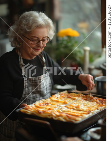 Elderly woman smiling while baking homemade lasagna in the kitchen with apron and cheese. Elderly woman smiling while baking homemade lasagna in the kitchen with apron and cheese. 123516627