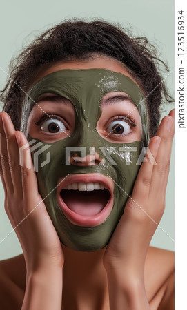 Surprised expression of a woman with a green facial mask for beauty and skincare treatment Surprised expression of a woman with a green facial mask for beauty and skincare treatment 123516934