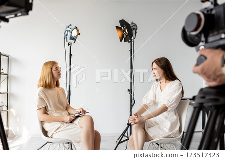 Studio conversation. Producer talk. Art director questions female model near cameras. Backstage video interview preparation photo shoot. Studio conversation. Producer talk. Art director questions female model near cameras. Backstage video interview preparation photo shoot. 123517323