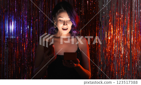 Surprise present. Festive night. Birthday party. Special day. Holiday magic. Amazed happy woman fancy dress open gift box on red shimmering cascade curtain background. Surprise present. Festive night. Birthday party. Special day. Holiday magic. Amazed happy woman fancy dress open gift box on red shimmering cascade curtain background. 123517388