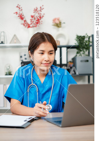 Female healthcare worker in blue scrubs using a laptop in a contemporary medical office environment. Female healthcare worker in blue scrubs using a laptop in a contemporary medical office environment. 123518120