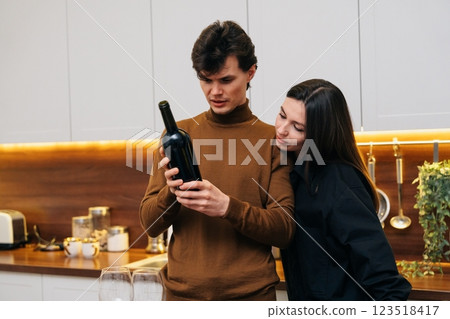 Young couple examines wine bottle in modern kitchen during evening gathering 123518417