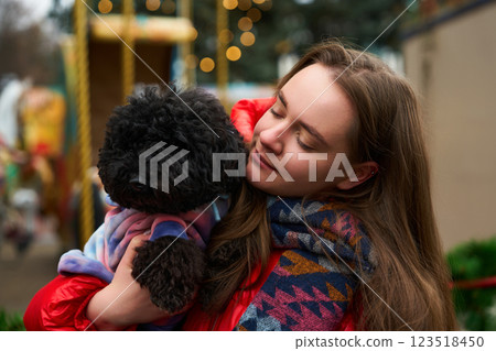 Young woman enjoys winter outing, holding fluffy black dog in warm scarf amidst festive decorations 123518450