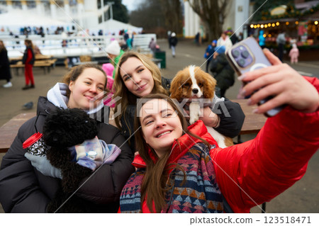 Friends enjoy a cheerful day at the park while taking selfies with their dogs during a festive winter event Friends enjoy a cheerful day at the park while taking selfies with their dogs during a festive winter event 123518471