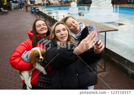 Friends taking a selfie with a dog by a fountain in a bustling outdoor location during winter Friends taking a selfie with a dog by a fountain in a bustling outdoor location during winter 123518557