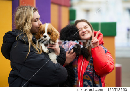 Two friends enjoy playful moments with their dogs in a colorful outdoor setting during a chilly afternoon Two friends enjoy playful moments with their dogs in a colorful outdoor setting during a chilly afternoon 123518560