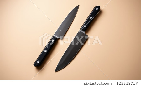 Two professional kitchen knives with sleek black handles lie against a golden backdrop, showcasing their sharpness and design, suitable for culinary brands or kitchen equipment marketing. 123518717