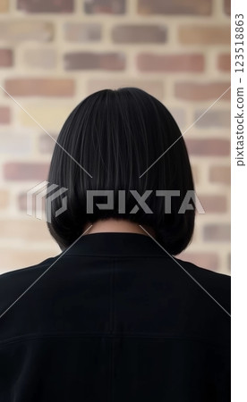 A sleek back view of a woman with neat black bob hair, styled elegantly, set against a rustic brick wall, perfect for showcasing fashion and modern hairstyles. 123518863