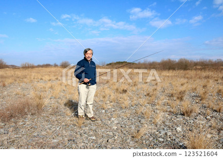 A veteran fisherman walking along the wide riverbed toward the current 123521604