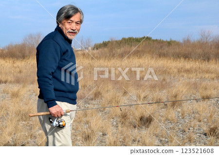 A veteran fisherman walking along the wide riverbed toward the current A veteran fisherman walking along the wide riverbed toward the current 123521608