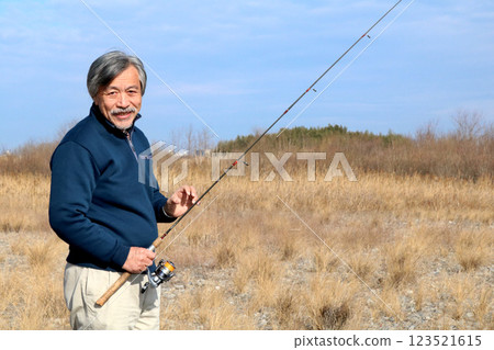 A veteran fisherman walking along the wide riverbed toward the current A veteran fisherman walking along the wide riverbed toward the current 123521615