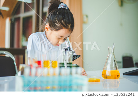 little scientist looking through a microscope and test tubes filled with chemicals for learning about science and experiments. little scientist looking through a microscope and test tubes filled with chemicals for learning about science and experiments. 123522241