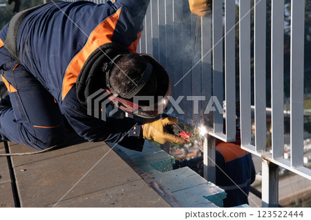 Industrial welder skillfully crafts a metal fence for a new business complex, using modern equipment that casts bright sparks and highlights the precision and dedication of the craft. 123522444