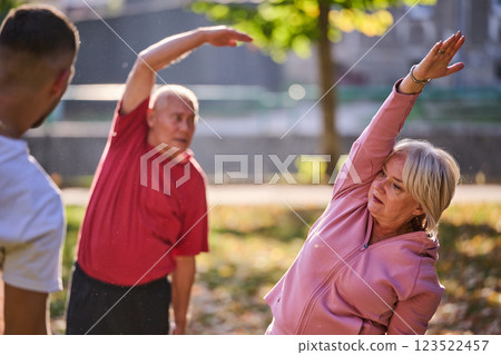 A group of seniors follows a trainer, engaging in outdoor exercises in the park, as they collectively strive to maintain vitality and well-being, embracing an active and health-conscious lifestyle in 123522457