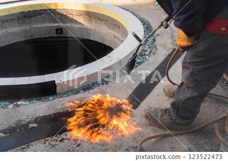 An industrial worker uses fire to soften a rubber underlay for floor insulation, showcasing precision and skill in a critical step of the construction process An industrial worker uses fire to soften a rubber underlay for floor insulation, showcasing precision and skill in a critical step of the construction process 123522473