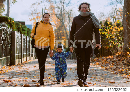A loving couple strolls through a sunlit park with their young son, surrounded by the vibrant colors of autumn, enjoying a joyful and peaceful family moment together. 123522662