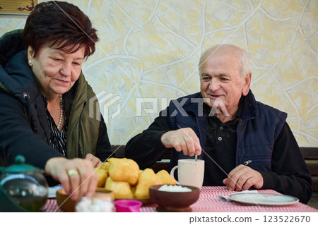 Elderly couple finds pure joy in the serene morning as they savor a cup of coffee, immersed in the tranquil beauty of nature that surrounds their rustic retreat 123522670