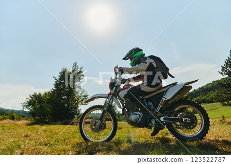 A motorcyclist equipped with professional gear, rides motocross on perilous meadows, training for an upcoming competition. 123522787