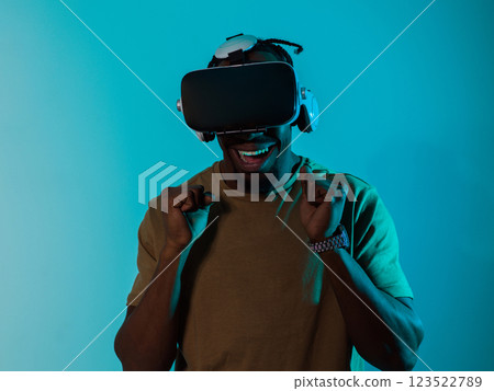 African American man immerses himself in a thrilling horror gaming experience using VR glasses, creating an isolated and intense atmosphere against a striking blue background 123522789