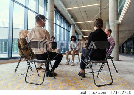 A diverse group of young business entrepreneurs gathered in a circle for a meeting, discussing corporate challenges and innovative solutions within the modern confines of a large corporation 123522798