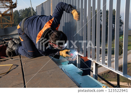 Industrial welder skillfully crafts a metal fence for a new business complex, using modern equipment that casts bright sparks and highlights the precision and dedication of the craft. 123522941