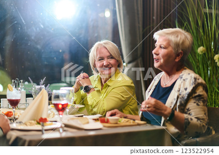 Elderly friends share a delightful dinner, filled with laughter, joy, and the warmth of enduring friendship, epitomizing the timeless pleasure of companionship in a contemporary setting 123522954