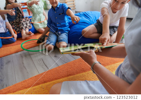A happy female teacher sitting and playing hand games with a group of little schoolchildren 123523012