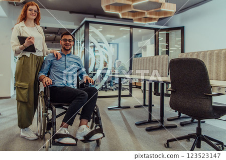 Young business colleagues, collaborative business colleagues, including a person in a wheelchair, walk past a modern glass office corridor, illustrating diversity, teamwork and empowerment in the Young business colleagues, collaborative business colleagues, including a person in a wheelchair, walk past a modern glass office corridor, illustrating diversity, teamwork and empowerment in the 123523147